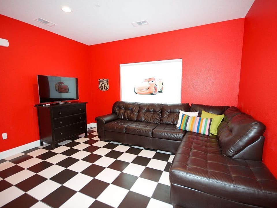 - Family lounge room with sectional sofa and large flat screen TV   - Bold red wall and checkered floor create a fun movie night vibe   - Comfortable space perfect for games, movies, and family relaxation