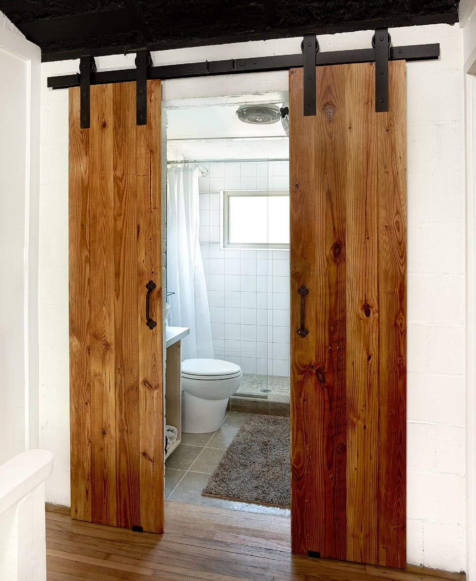 Rustic bathroom door leads to a modern bathroom with a walk-in shower.