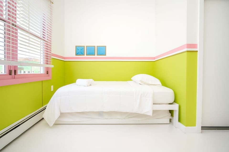 Cheerful bedroom with bright green walls, cozy bed, and fresh white linens—sunny, clean, and welcoming for a comfortable stay.
