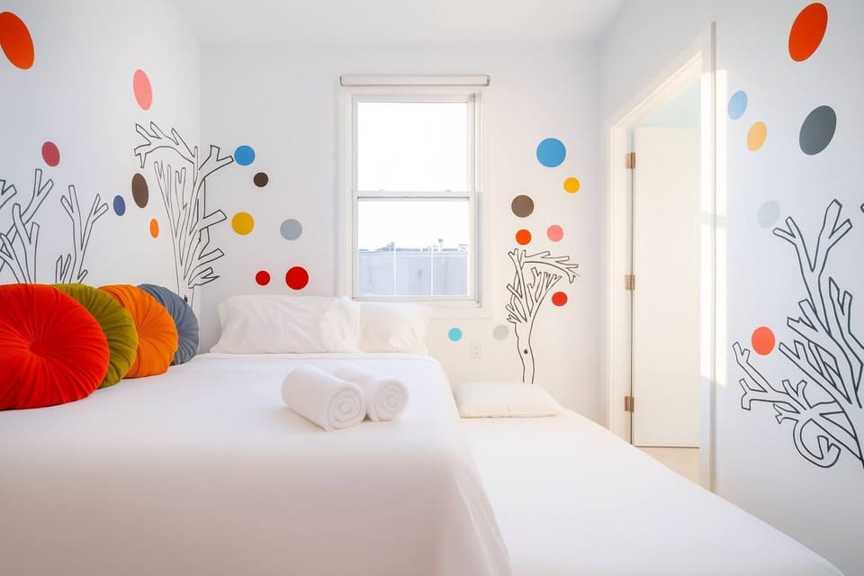 Bright, whimsical bedroom with playful wall art, cozy bed, and natural light—clean, cheerful, and uniquely designed.
