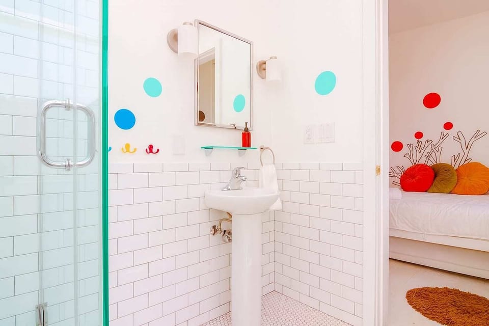 Bright, modern bathroom with subway tile and glass shower, plus peek into playful bedroom—clean, fresh, and thoughtfully designed.

