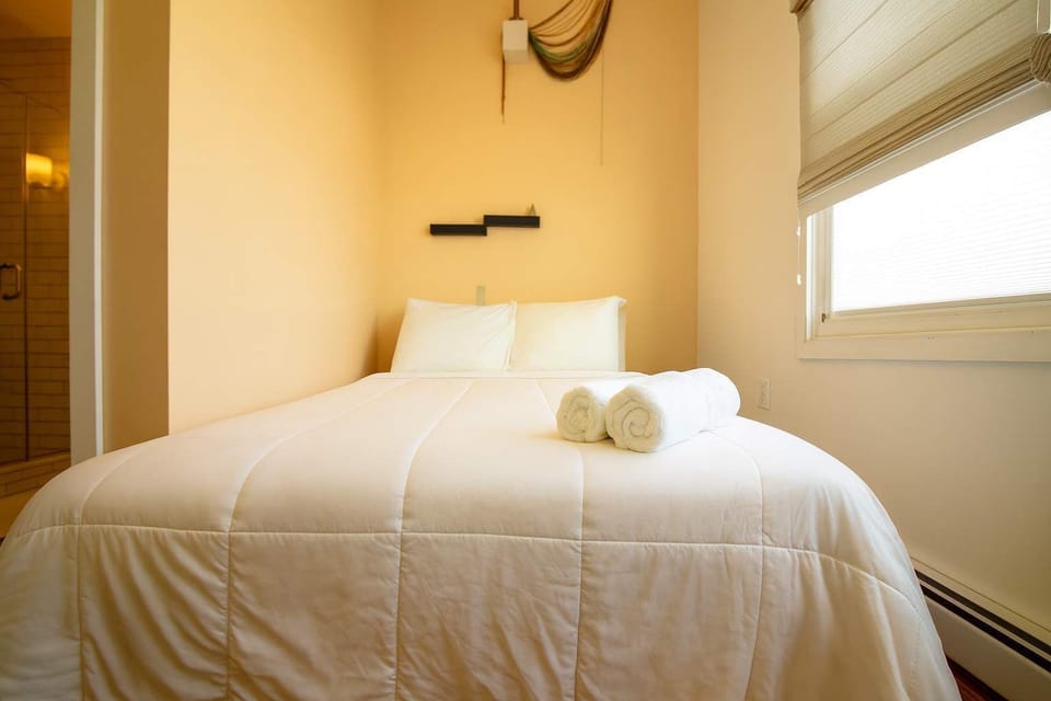 Cozy, sunlit bedroom with plush white bedding, rolled towels, and warm tones—clean, comfortable, and ideal for a relaxing stay.
