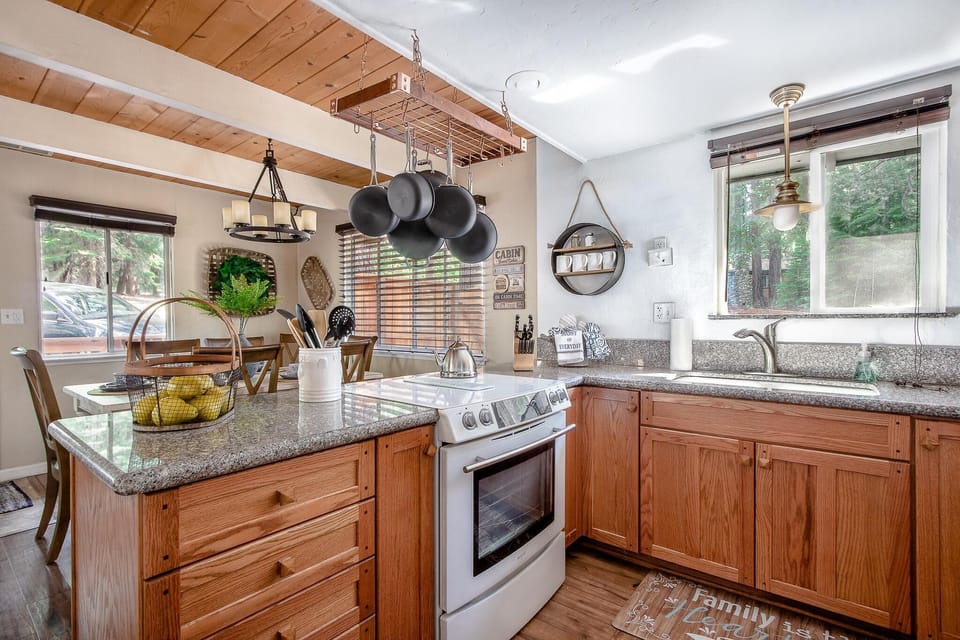 Granite countertops and oak cabinets surround a white stove and stainless steel sink beneath a pendant light.