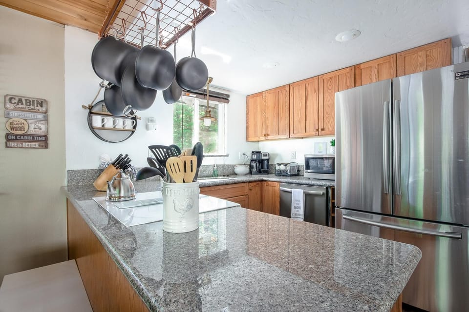 Kitchen with granite countertops, oak cabinets, stainless steel appliances, and hanging black cookware rack.