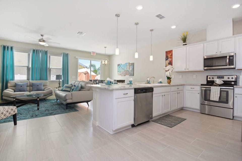 Relax in this bright open-plan living area with coastal teal accents, comfy sofas, modern tile floors and a roomy kitchen island - a welcoming spot to unwind after a day of exploring.