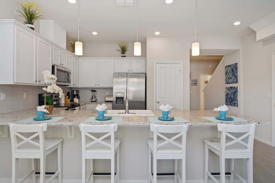 Bright modern kitchen with white cabinets, granite island, pendant lights and a breakfast bar that seats four-stainless-steel appliances make cooking a breeze.
