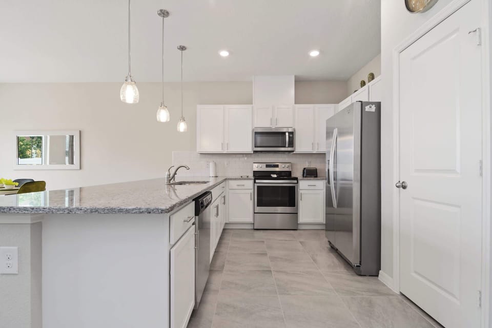 Spotless U-shaped kitchen with granite counters, stainless fridge & oven, subway-tile backsplash and ample white cabinetry-clean, contemporary style for effortless meal prep.