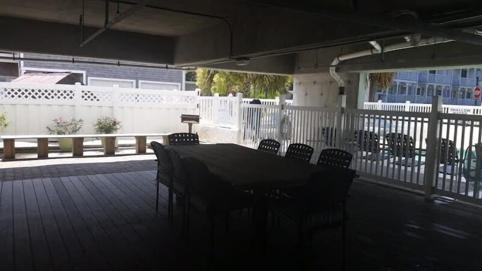 Parking level includes patio with table and chairs and grill next to pool.