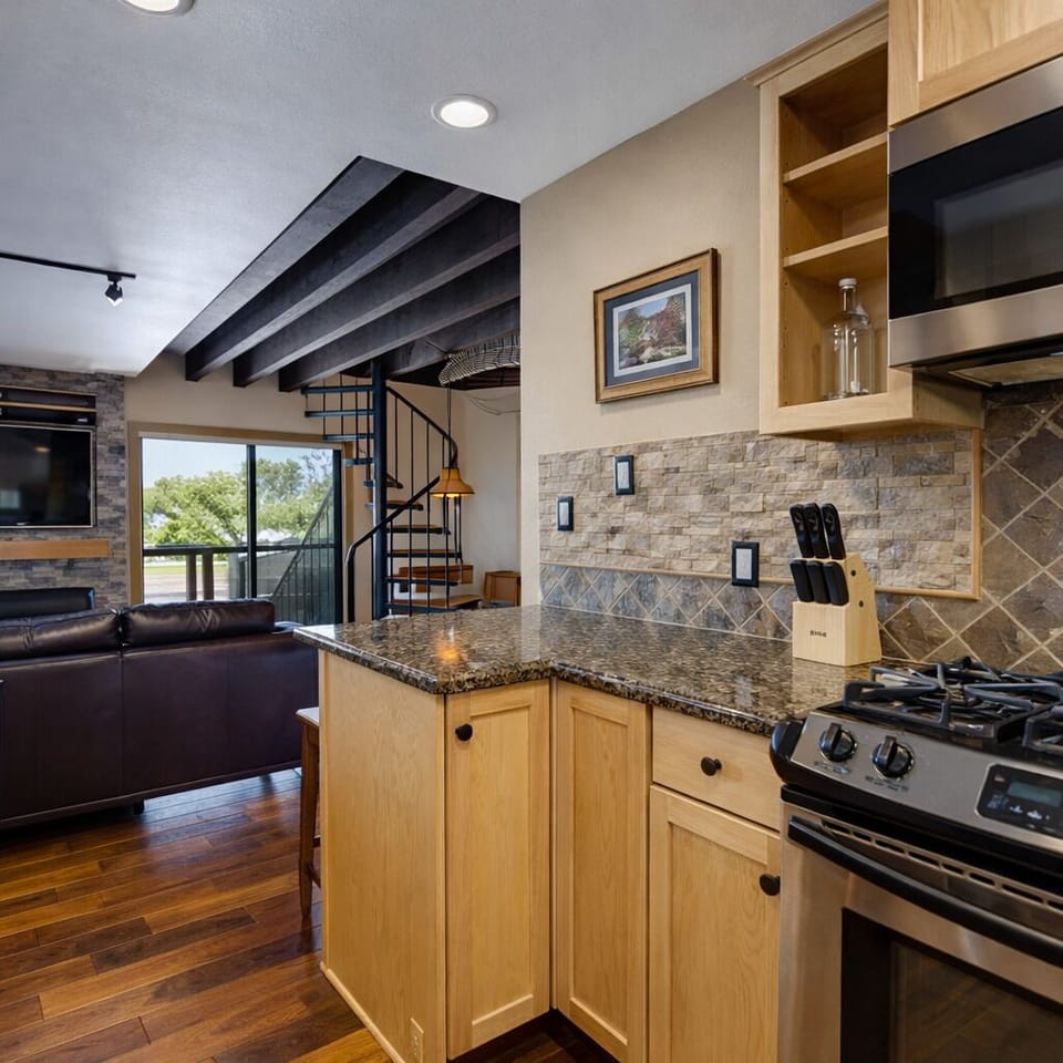 Compact kitchen with granite countertops, stainless steel appliances, and a unique spiral staircase nearby. Perfect for your mountain escape.