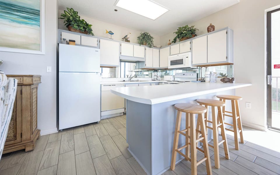 Prepare meals in the bright kitchen featuring a spacious island and seating, surrounded by charming decor and greenery