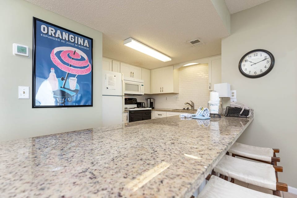 The kitchen features granite countertops, modern appliances, and a vibrant vintage poster, perfect for meal prep or gathering