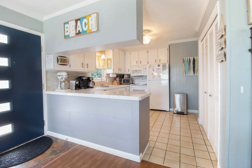 Your beach-themed kitchen offers a bright open layout with white cabinetry, stainless appliances, and a breakfast bar—perfect for whipping up your morning coffee or a quick snack between ocean dips.