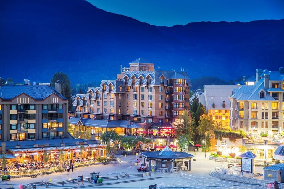 Charming village square illuminated by soft evening lights, framed by majestic mountain silhouettes.