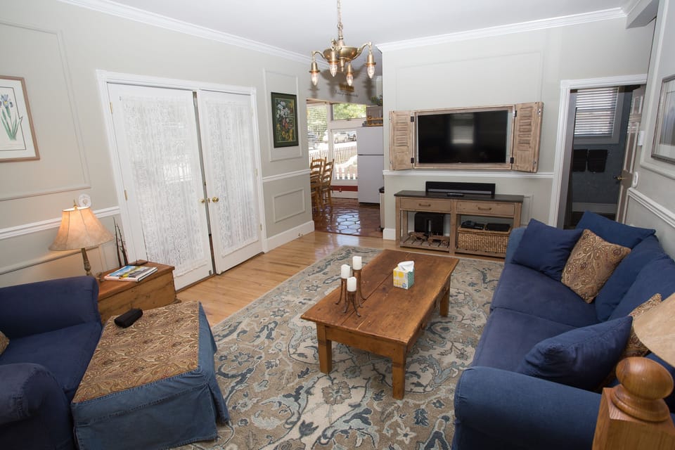 Living room with large screen TV and sound bar. Double doors enter the sun room.