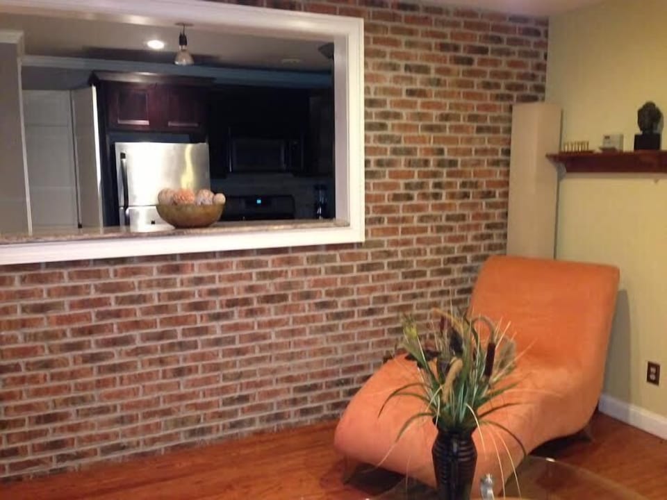 Beautiful brick wall separating kitchen from living room. Lovely  chaise.