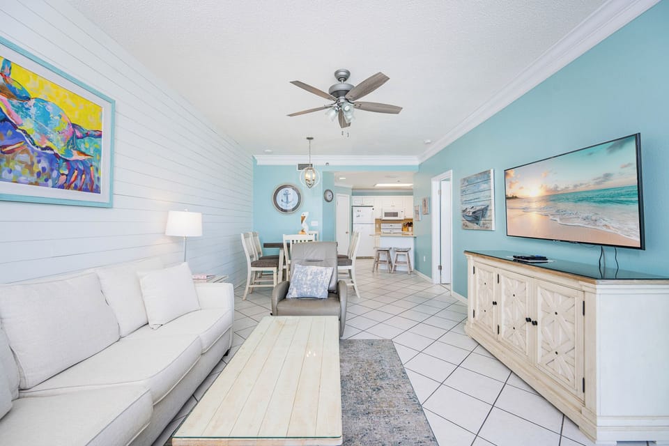 Open living area featuring a light sofa with queen sleeper, beach artwork, and a large TV, for a cozy family retreat