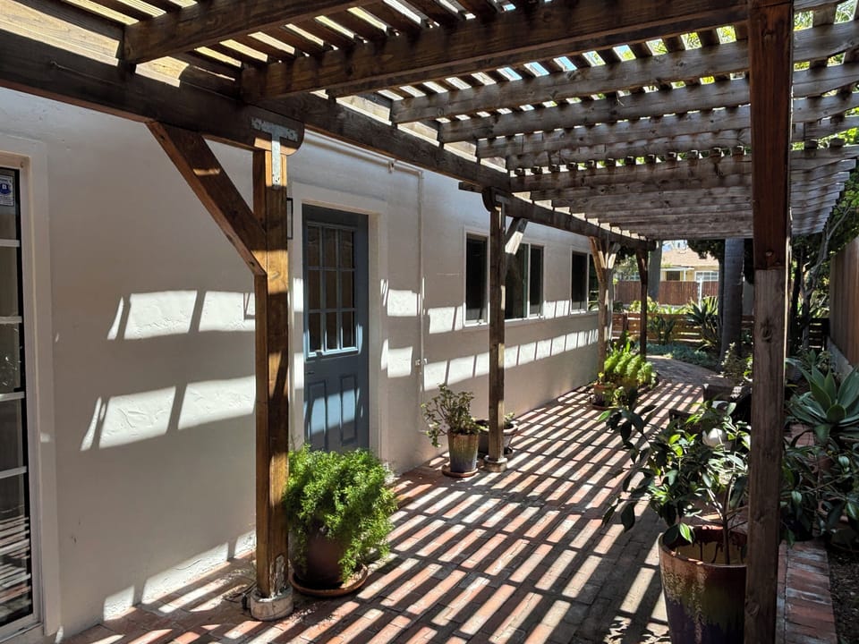 Charming front patio with a sun-dappled pergola and lush coastal greenery.