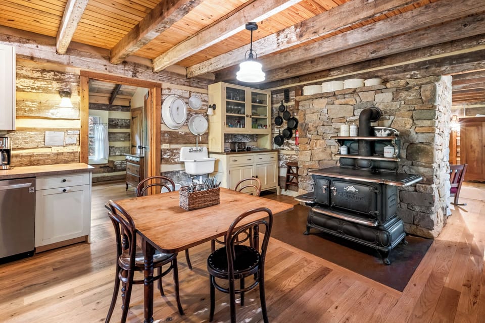 Kitchen with antique restored cast-iron wood stove.  Modern electric range at left (not visible in photo).  Kitchen is arranged in old-fashioned manner with table in middle and cabinets and appliances at walls.