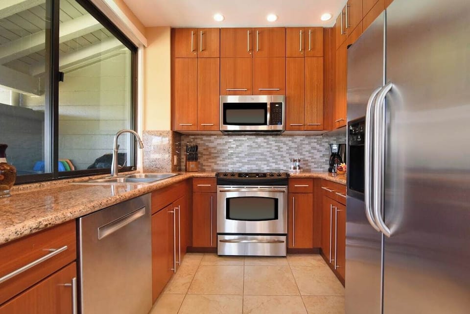 Fully equipped kitchen with stainless steel appliances, granite countertops, custom wood cabinetry, and modern lighting.
