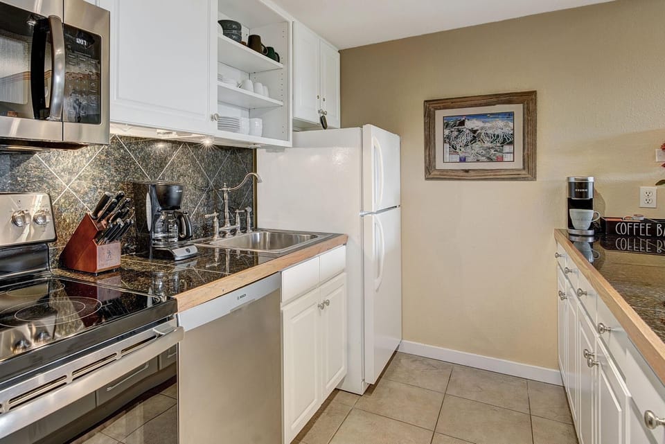 Dark granite countertops and backsplash contrast with white cabinetry and stainless steel appliances in the kitchen.