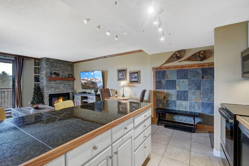 Black granite kitchen island overlooks stone fireplace and TV in open living area with slate-tiled entry bench.