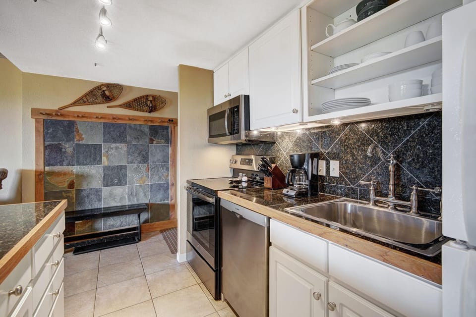 Black granite countertops and backsplash complement stainless steel appliances and white cabinetry in the kitchen.