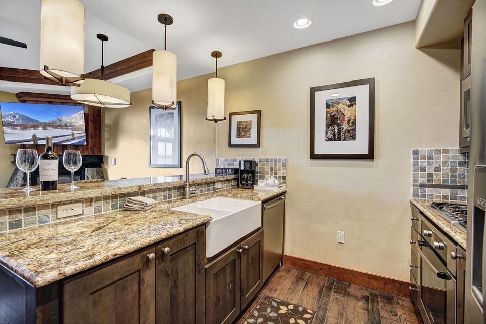 Granite countertops extend along the kitchen with a farmhouse sink, mosaic tile backsplash, and pendant lights.