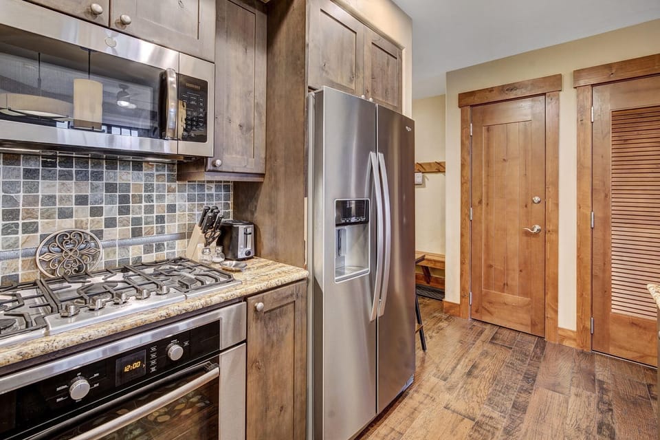Slate tile backsplash and wood cabinetry surround stainless steel appliances in the kitchen.