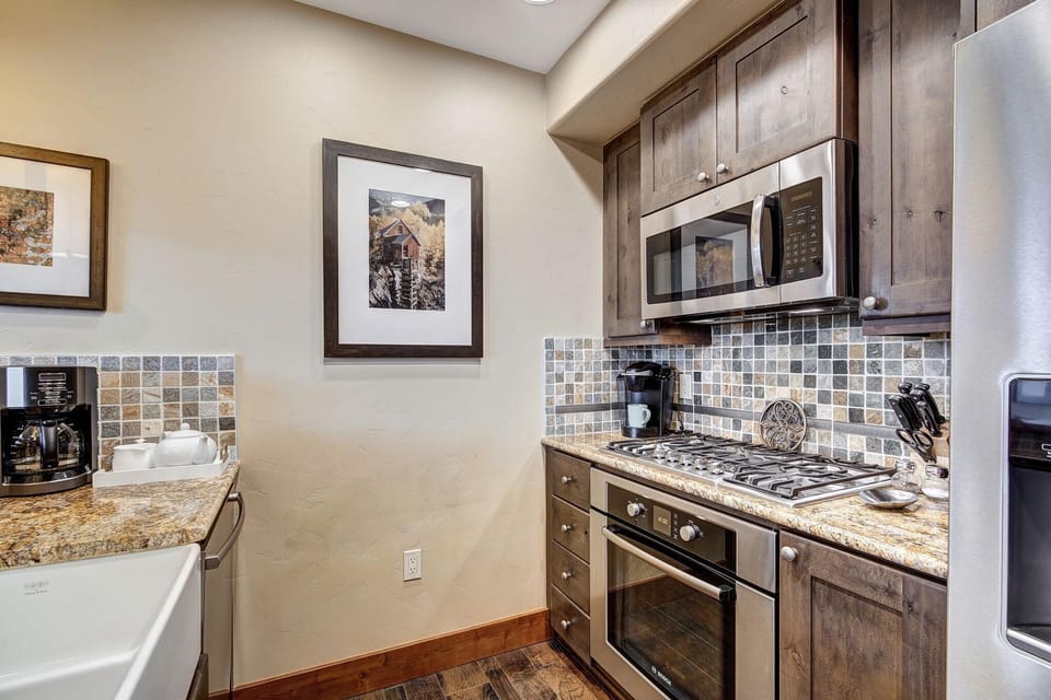 Gas cooktop and stainless steel microwave are set above granite counters with mosaic tile backsplash.