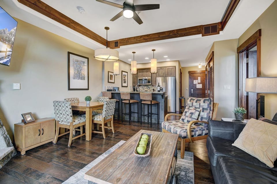 Open-concept living and dining area with patterned armchair, leather sofa, and wood flooring under warm lighting.