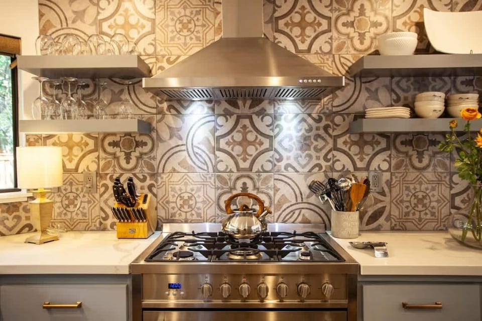 Charming, fully equipped kitchen featuring a stainless-steel gas range, stylish patterned tile, and open shelving. Warm lighting and modern finishes create an inviting space perfect for cooking and gathering.