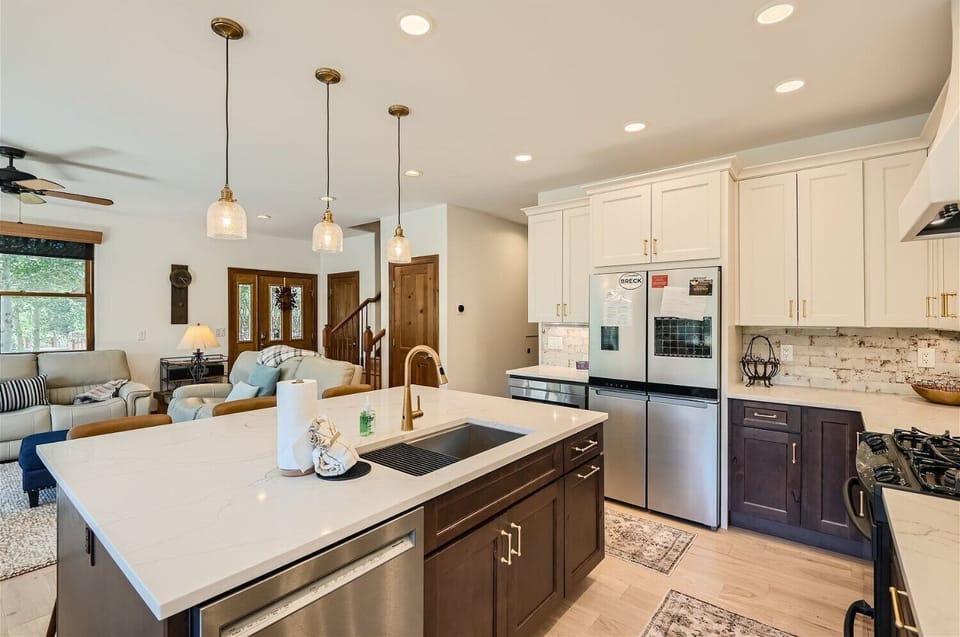 Modern kitchen with a central island featuring a sink and paper towel holder. Stainless steel refrigerator, white upper cabinets, and dark lower cabinets. Open layout with a view of the living area.