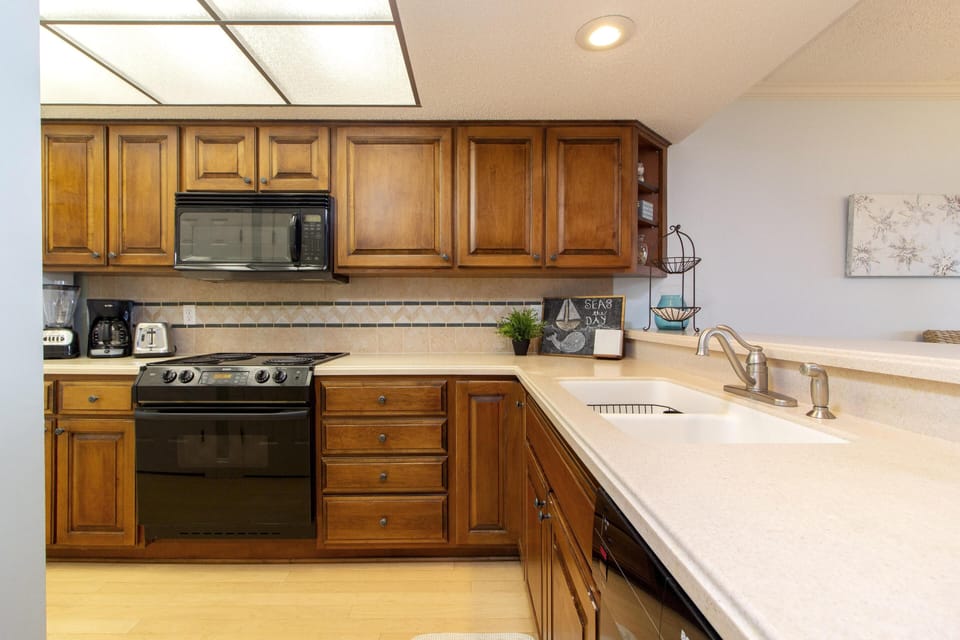 Kitchen with honey-toned wood cabinets, black appliances, beige tile backsplash, and creamy quartz countertops.