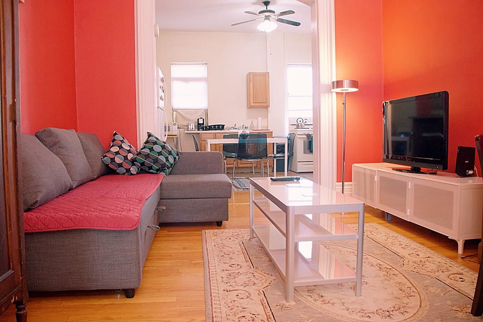Sofa bed, coffee table, TV and TV stand, floor lamp. Kitchen area in the back.
