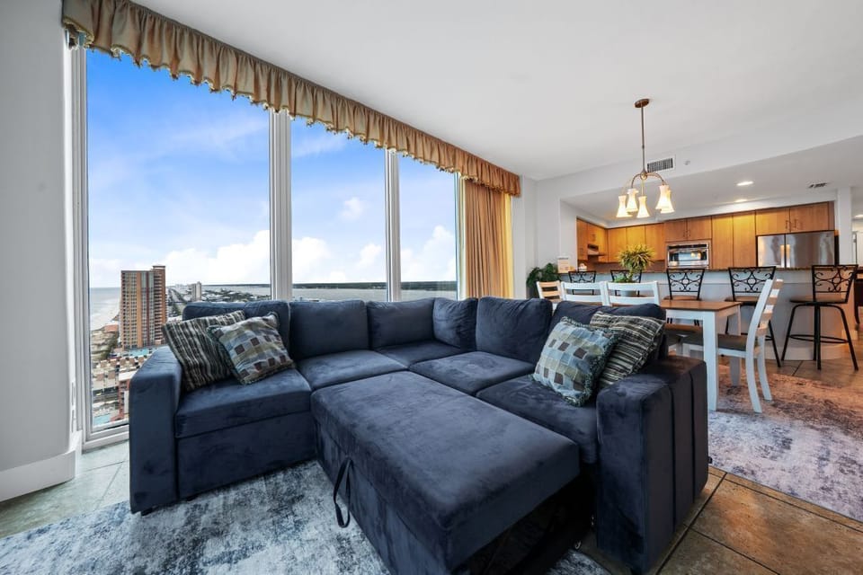 Unwind on the plush sectional sofa while enjoying panoramic water views through floor-to-ceiling windows in this elegant open-concept living space.