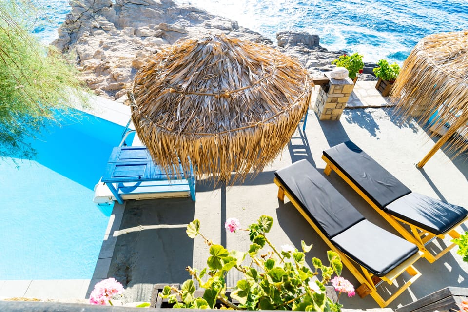 Swimming pool, wooden sun beds, wicker umbrellas, Ikarian rocks, Aegean sea.