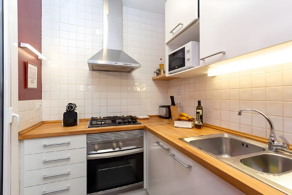 The modern kitchen boasts stainless steel appliances, including an oven, stovetop, and range hood. The wooden countertop is perfect for preparing meals and features a double sink with a sleek chrome faucet.