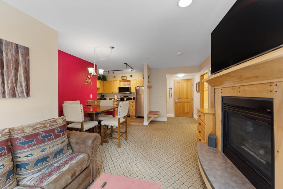 The living area offers a mounted TV over a gas fireplace, a queen sleeper sofa, and access to the balcony.