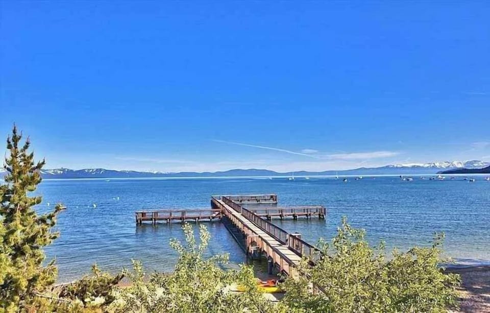 Lake view with dock, beach, boats, mountains, and trees along the shoreline.