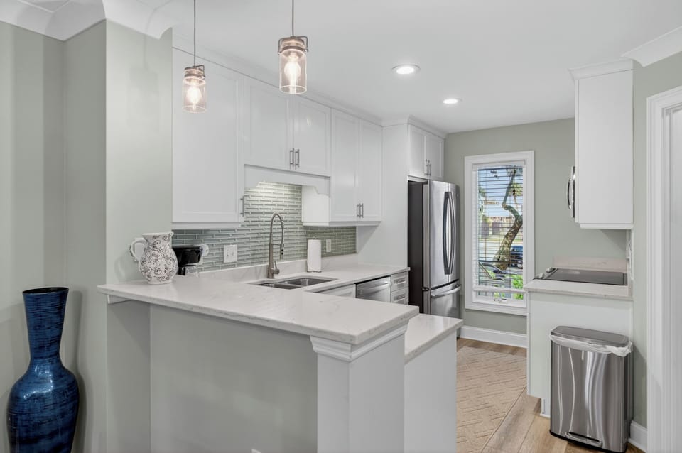 Bright, modern kitchen featuring white cabinetry, gleaming countertops, and stainless appliances—your perfect space to create delicious meals during your stay.