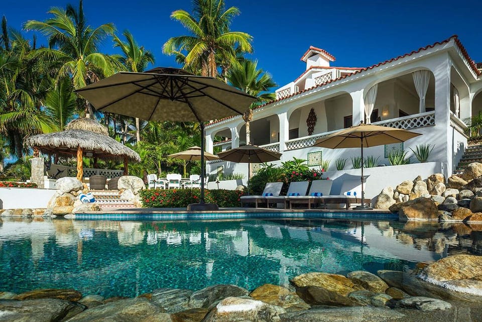 Pool deck with palapa shade, sun loungers and umbrellas at Casa Edwards, beachfront villa in Palmilla