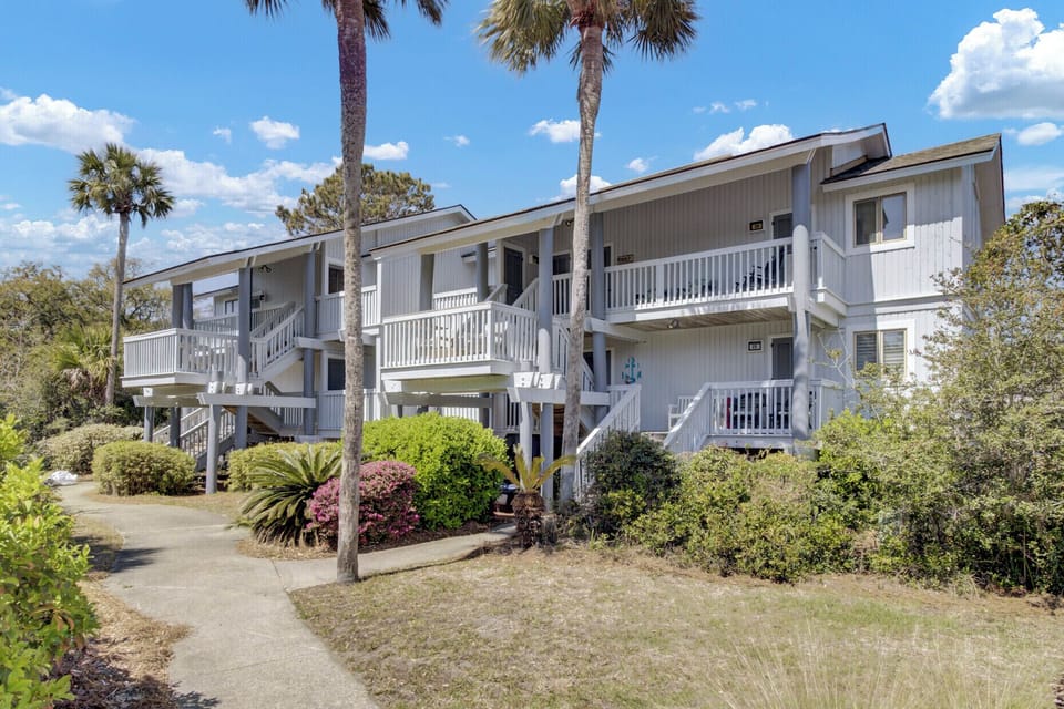 Charming coastal condo complex with private balconies, landscaping, and classic palm lined walkways.