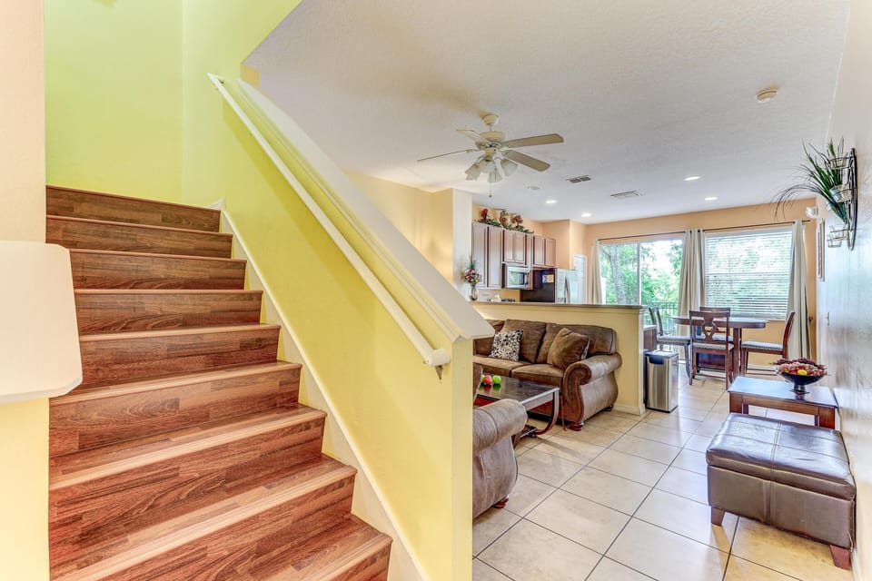 Tile flooring extends through the living room and dining area with wood stairs rising alongside a pale yellow wall.