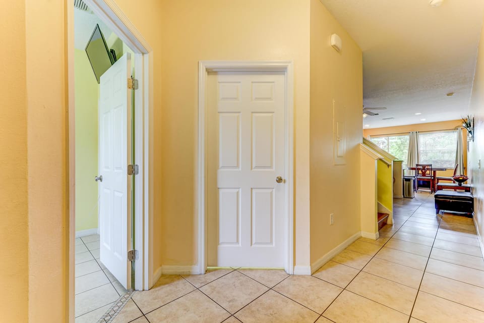View into bedroom with wall-mounted TV seen through open white door, alongside tiled hallway and staircase.