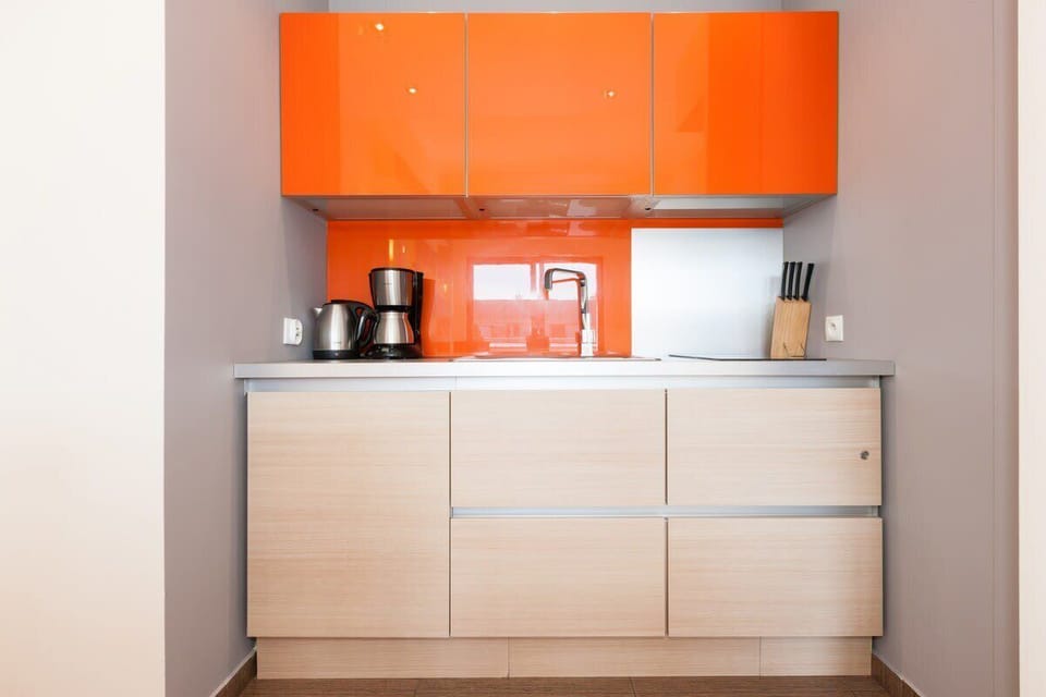  A close-up of the kitchen, featuring sleek, minimalist cabinetry in white and orange tones, with essential appliances.