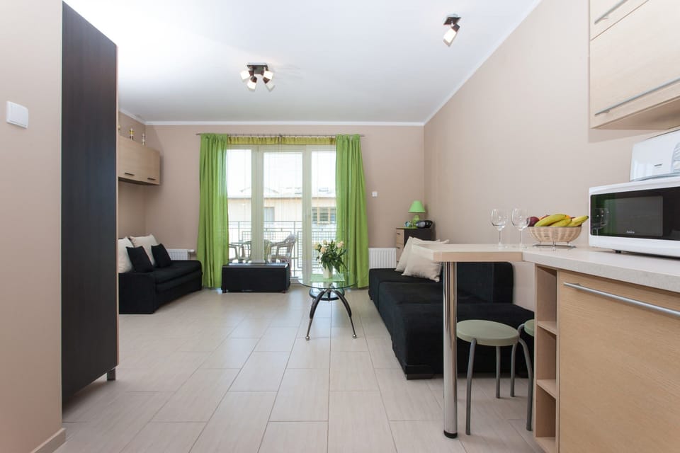 This view shows a narrow perspective of the living space and kitchen, with the black couch on one side and the open kitchen area with a dining table at the back.