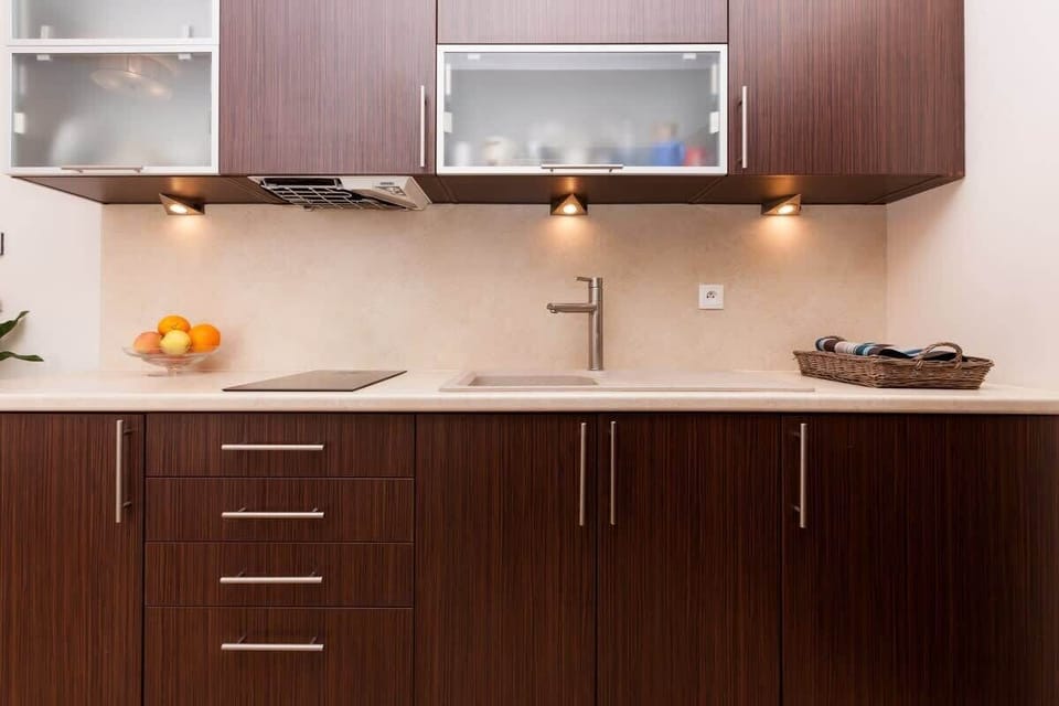 A kitchen area featuring dark brown cabinets and a clean, minimalistic design. The lighting under the cabinets adds a modern touch.