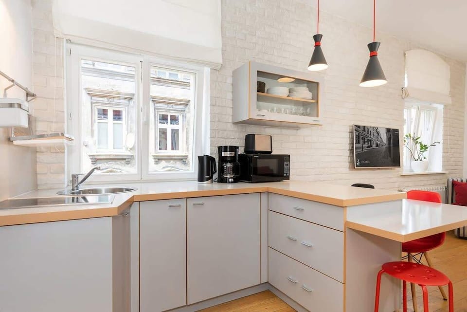 A modern kitchenette with light grey cabinets and a sleek white backsplash. The space is compact but efficient, featuring stainless steel appliances and a wooden countertop that adds warmth to the room.