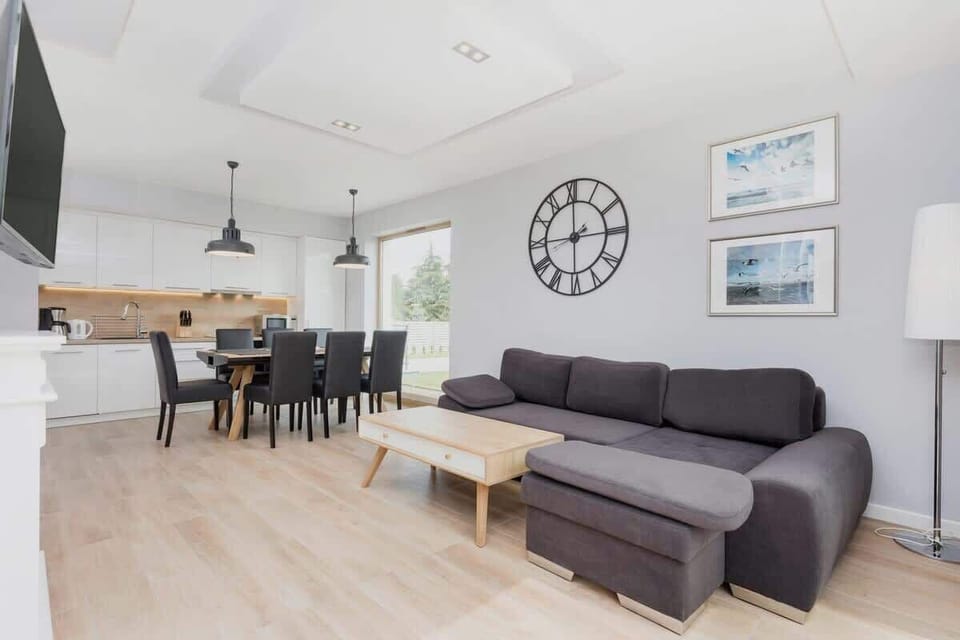 A dining area in a modern open-plan living space, with a black table and chairs, large windows, and minimalist decor, giving it a sophisticated yet welcoming feel.