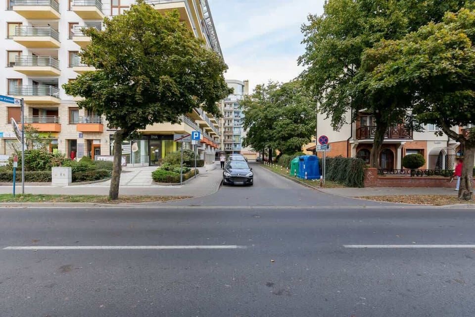 A quiet street lined with residential buildings, trees, and parked cars, offering a calm, urban atmosphere.